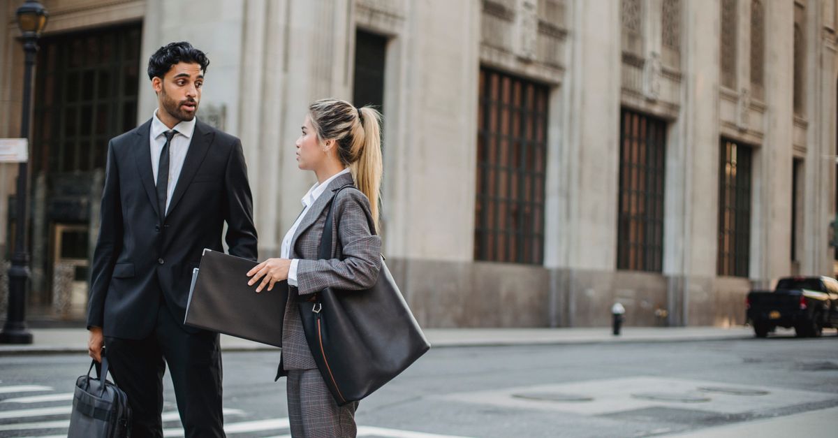 Two business professionals discuss on a city street, showcasing formal attire and urban setting.